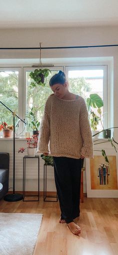 a woman standing in front of a window wearing a sweater and slip ons with her feet crossed