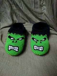 a pair of green and black slippers with an angry grin face on the front