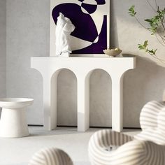 a white table sitting next to a vase on top of a wooden table in front of a painting