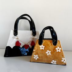 two purses sitting next to each other on top of a white table with black handles