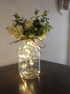 a mason jar filled with white flowers and fairy lights on a wooden table next to a wall