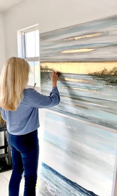 a woman is painting an ocean scene on a canvas