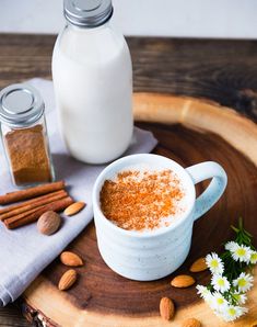 a cup of cinnamon spice next to a bottle of milk on a wooden tray with flowers