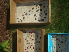 two boxes are sitting on the grass and one is filled with different colored glass beads