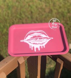 a pink tray with white lips on it sitting on top of a wooden rail outside