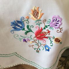 an embroidered piece of cloth with flowers and leaves on the front, sitting on a table