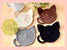 four crocheted cat coasters sitting on top of a table next to a coffee cup