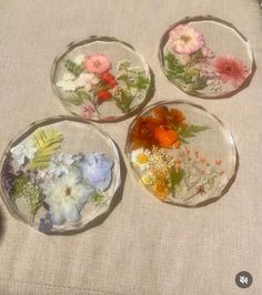 four glass plates with flowers in them sitting on a cloth covered tablecloth next to a vase