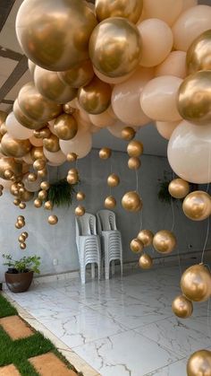 gold and white balloons are hanging from the ceiling in an outdoor space with lawn chairs