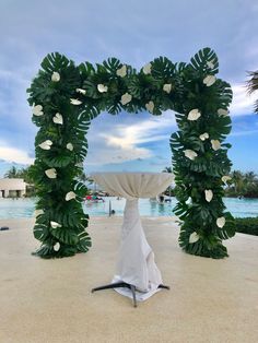 an arch made out of leaves and flowers with a fountain in the background at a resort