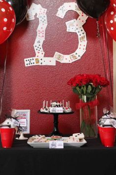 a table topped with lots of red roses and black balloons next to a sign that says 13