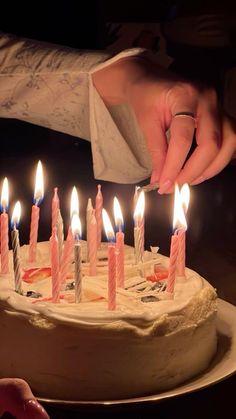 a person lighting candles on a cake with white frosting and pink icing in the middle