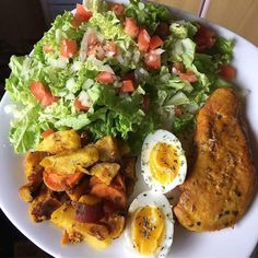 a white plate topped with meat, salad and an egg next to fried chicken on a bed of lettuce