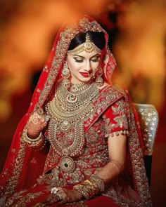 a woman in red and gold bridal outfit sitting down with her hands on her chest