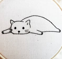 a white cat laying down on top of a table next to a cross stitch hoop