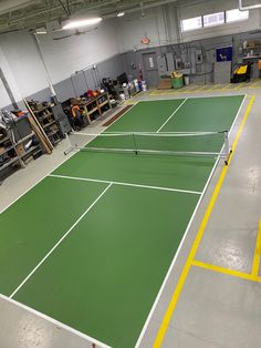 an indoor tennis court with green and yellow lines on the floor, surrounded by other equipment