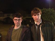 two young men standing next to each other in front of a car at night time