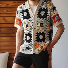 a man standing in front of a wooden wall wearing shorts and a crocheted shirt