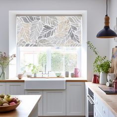 a kitchen with white cabinets and an open window covered in leafy blinds over the sink