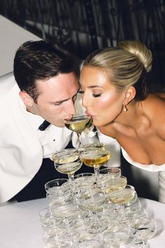 a bride and groom kissing while drinking wine from glasses on a table with champagne flutes in front of them