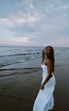 a woman standing on top of a beach next to the ocean with her eyes closed