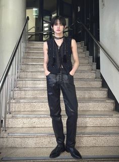 a young man standing in front of some stairs wearing leather pants and a black top