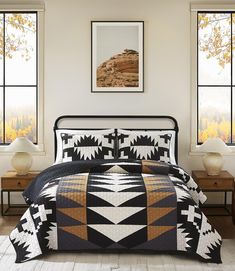 a bed in a room with two windows and a black and white quilt on the bed