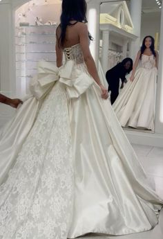 a woman in a wedding dress is looking at herself in the mirror while another person looks on