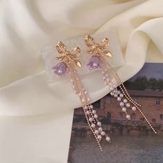 Gorgeous purple lily flower and gold bow layering tassel dangly statement earrings. Adorable lilac bohemian floral charm combined with delicate gold bow, with double pearl beads and double gold chains dangles. Super cute dainty feminine earrings, absolutely unique and eye catching! 💎 Features: ♥ Handcrafted Jewelry ♥ Material: Finest 14K Gold plated ♥ Main stone: Resin ♥ Side Stone: cultured pearl ♥ Approximate Measurements: - Length: 3.2" - Width: 0.8" ♥ Lightweight, easy to wear ♥ Nickel/Lead Purple Lily Flower, Purple Statement Earrings, Tulip Earrings, Purple Lily, Lavender Earrings, Feminine Earrings, Flower Earrings Gold, Tassel Earing, Princess Earrings