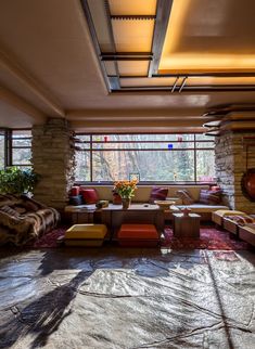 a living room filled with lots of furniture next to a large window on top of a stone wall