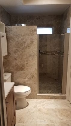 a bathroom with a walk in shower next to a white toilet and sink under a window