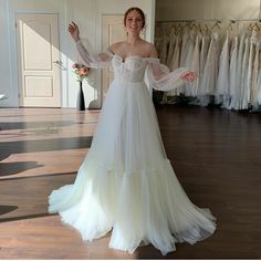 a woman standing in front of a rack of wedding gowns with her arms out