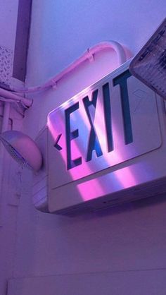 an exit sign is lit up with purple light in the background and on top of a white wall