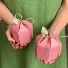 two hands holding pink paper boxes tied with twine