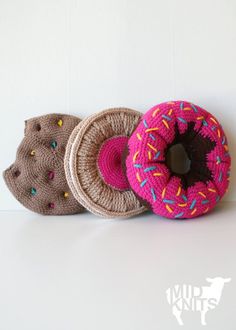 three crocheted donuts with sprinkles are lined up against a white wall