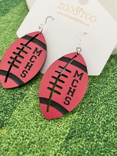 the football earrings are on display in front of a card and some green grass with a tag