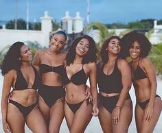 four women in black bikinis posing for a photo on the beach with palm trees behind them