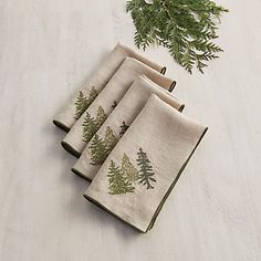 four napkins with pine trees on them are sitting on a table next to evergreen branches