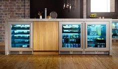 two refrigerators with glass doors on each side in a kitchen area next to a brick wall