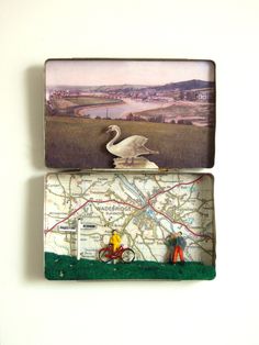 two small tin boxes with miniature figurines in them, one holding a swan and the other carrying a bicycle