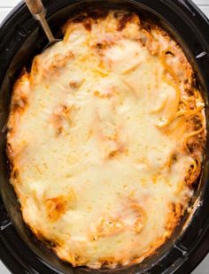 a casserole dish with cheese and meat in a black crock pot on a white table