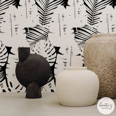 two vases sitting next to each other in front of a wall with black and white designs