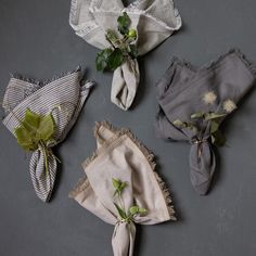 four cloth napkins with flowers and leaves tied to them on a gray surface,