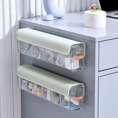 two clear plastic drawers on top of a gray desk next to a white computer monitor