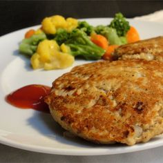 two crab cakes on a white plate with broccoli and cauliflower in the background