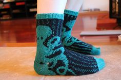 the legs of a person wearing socks with blue and green designs on them, standing in front of a television