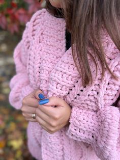 a close up of a person wearing a pink sweater and holding a cell phone in their hand