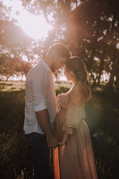 a pregnant couple standing in the grass at sunset