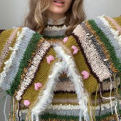 a woman with blonde hair wearing a multicolored knitted poncho and sweater