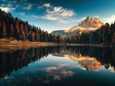 a mountain is reflected in the still water of a lake surrounded by pine trees and evergreens